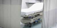 View through privacy curtains to empty hospital bed
